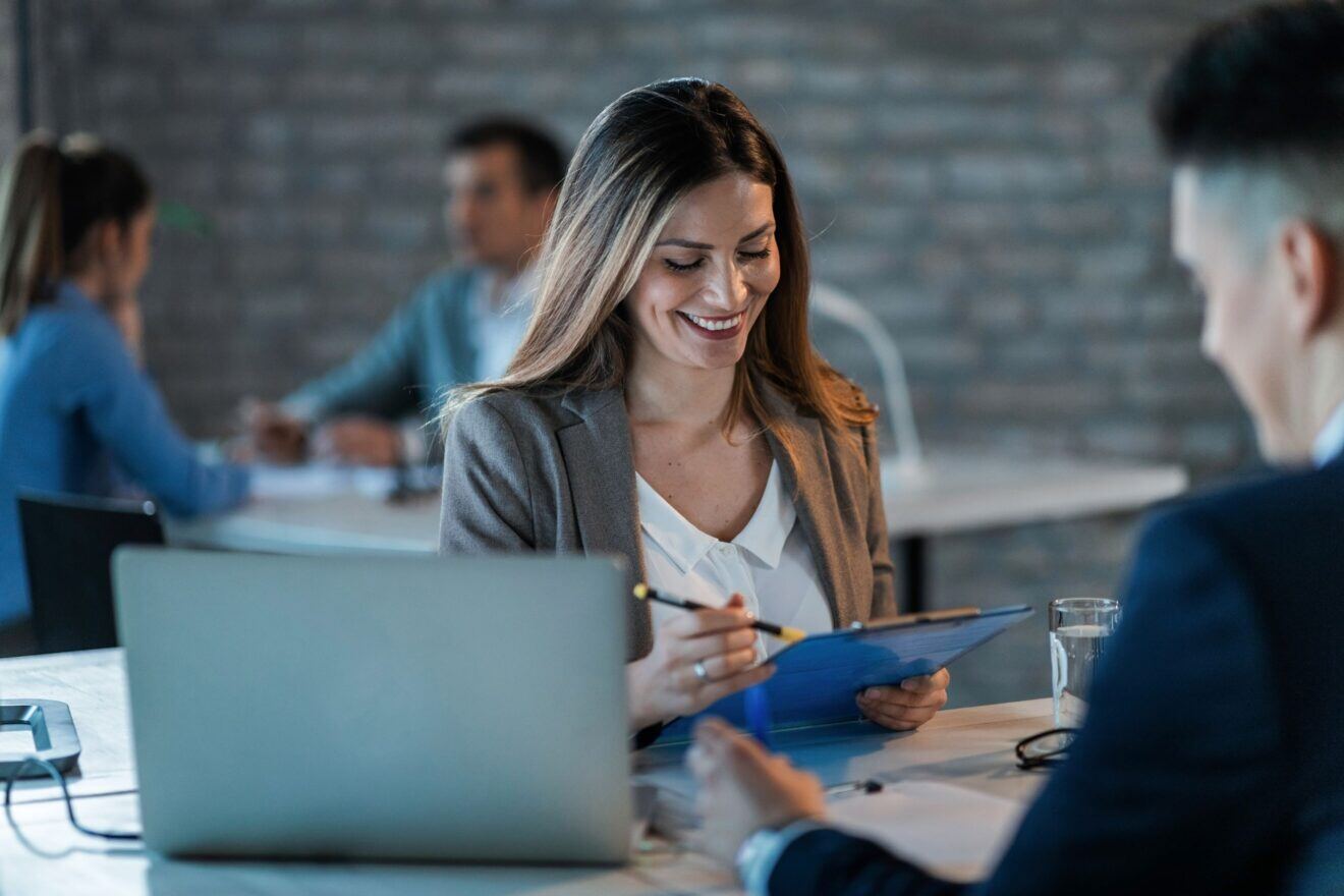 young-happy-businesswoman-reading-reports-while-going-through-paperwork-working-with-colleague-office-1320x880